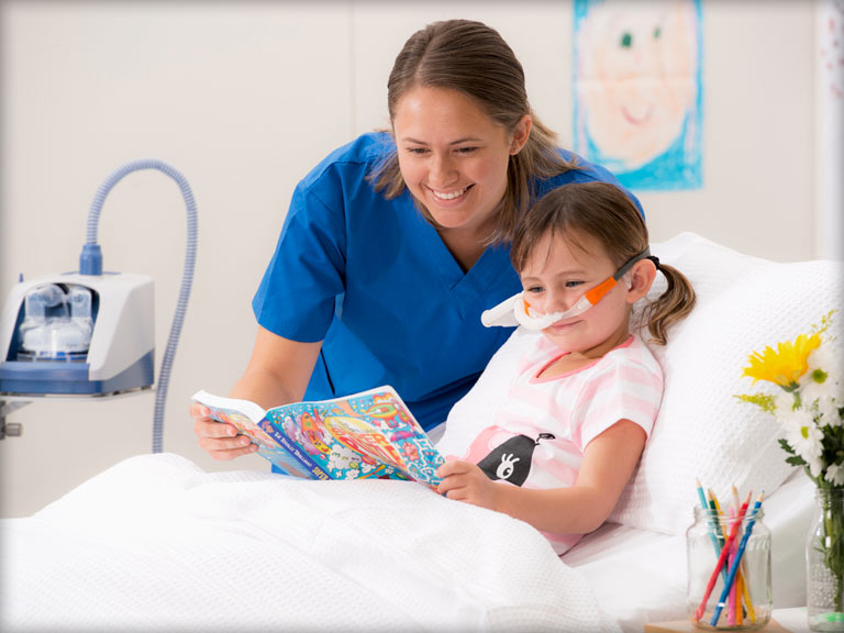 背景图片为一名护士正陪伴一名使用F&P Airvo 呼吸湿化治疗仪的儿童在看书